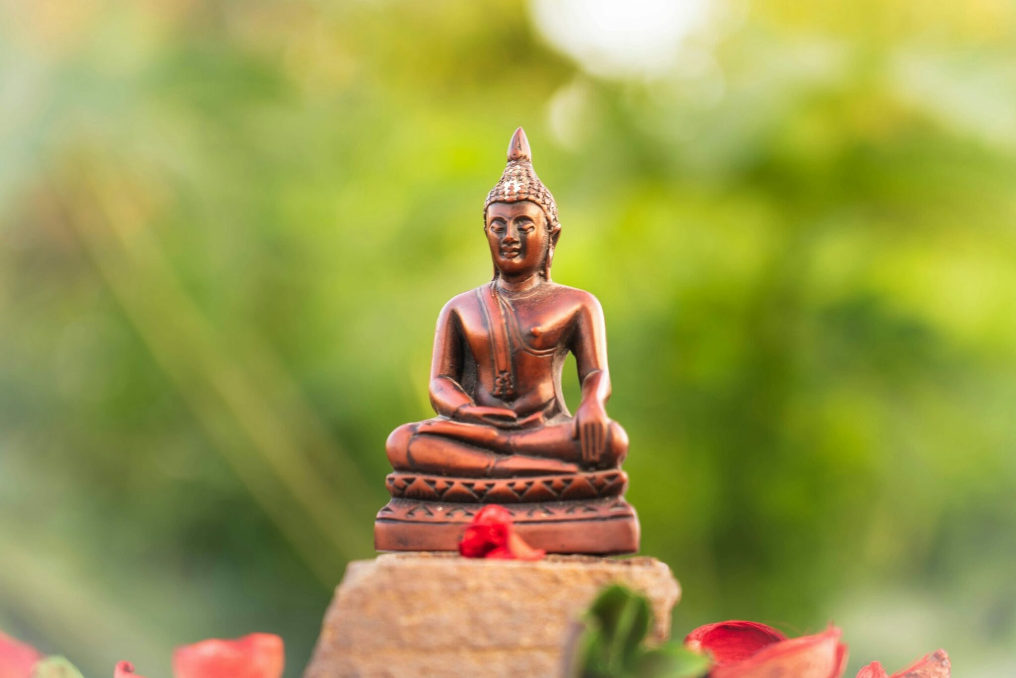Bronze Buddha Statue Surrounded by Flowers and Green Background